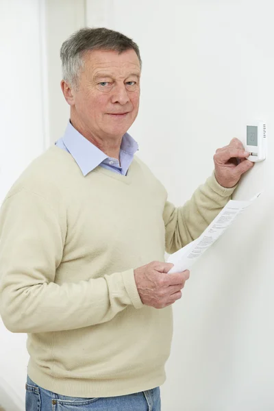 Worried Senior Man With Bill Turning Down Heating Thermostat