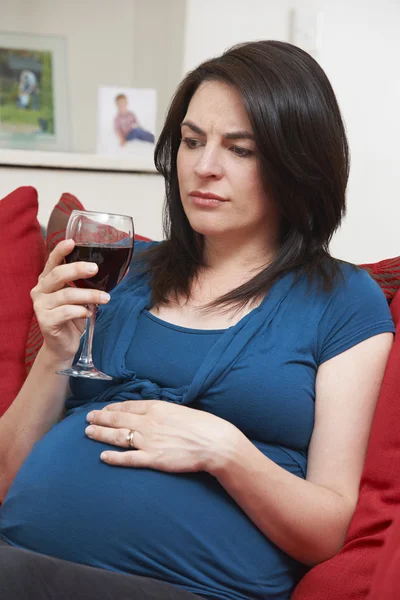 Concerned Pregnant Woman Drinking Glass Of Wine At Home