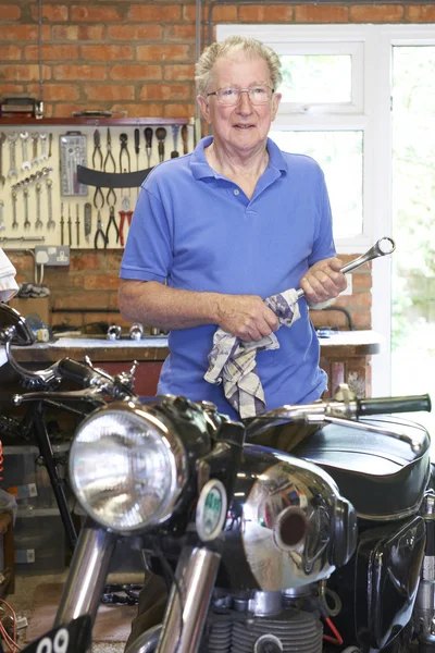 Senior Man Restoring Vintage Motorcycle In Garage
