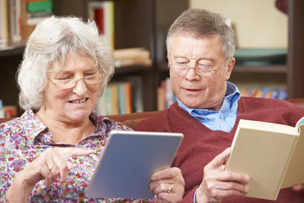 Senior Couple Using Digital Tablet And Reading Book