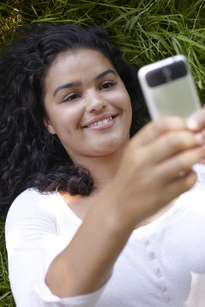 Young Woman Lying On Grass Sending Text Message