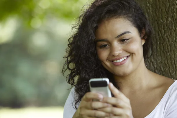 Young Woman Sitting In Park Sending Text Message