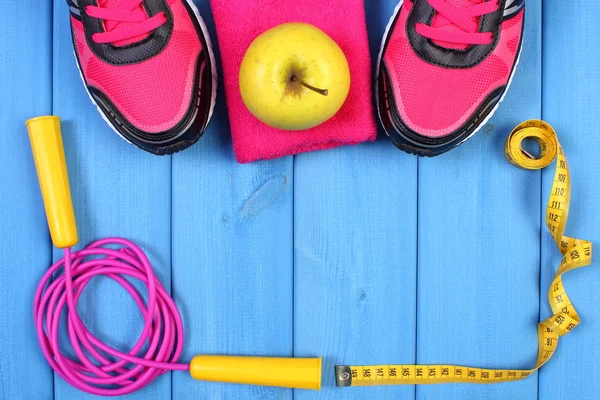 Pair of sport shoes, fresh apple and accessories for fitness on blue boards copy space for text