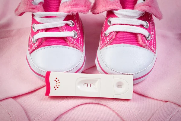 Pregnancy test with positive result and clothing for newborn, expecting for baby
