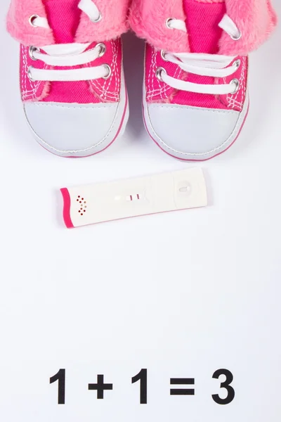 Pregnancy test with positive result and baby shoes on white background, expecting for baby, copy space for text