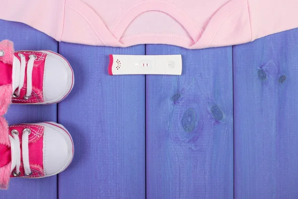 Pregnancy test with positive result and clothing for newborn, expecting for baby, copy space for text
