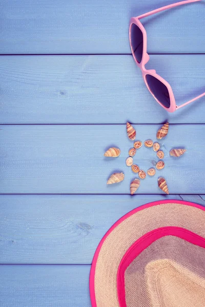 Seashells in shape of sun, sunglasses and straw hat on blue boards, accessories for summer, copy space for text