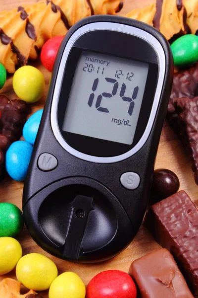 Glucose meter with heap of sweets, diabetes and unhealthy food