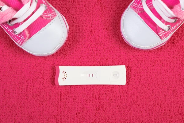 Pregnancy test with positive result and baby shoes on fluffy towel, expecting for baby