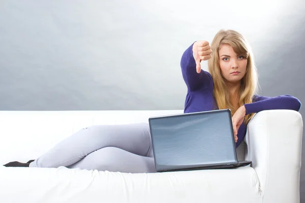 Unhappy woman with laptop sitting on sofa and showing thumbs down, modern technology