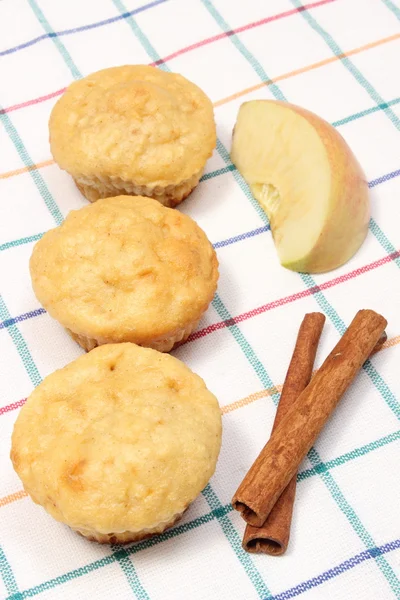 Baked muffins, fresh apple and cinnamon sticks on colorful cloth
