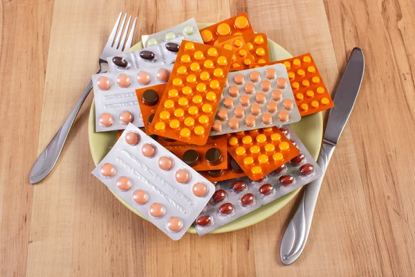 Blisters of tablets or supplements on plate and fork with knife, health care concept