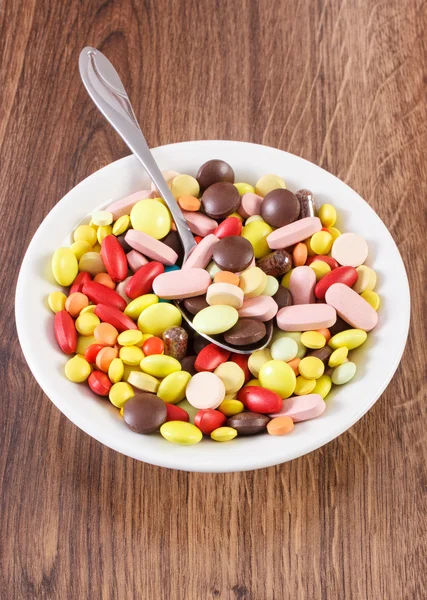 Medical pills on teaspoon and heap of colorful medical capsules on plate, health care concept