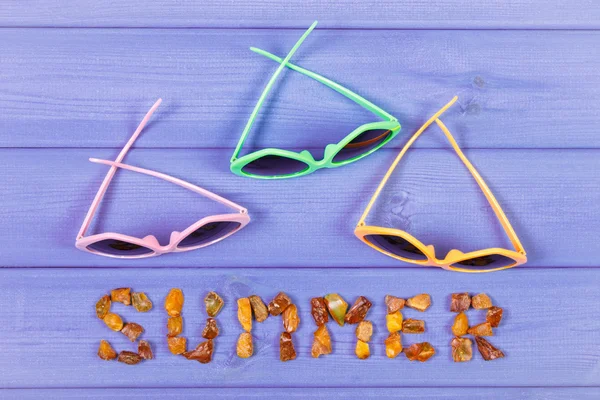 Word summer made of amber stones and sunglasses on purple boards, summer time