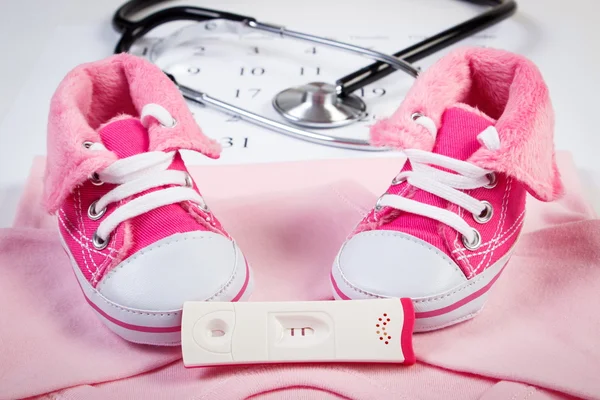 Pregnancy test with positive result, clothing for newborn and stethoscope on calendar, expecting for baby