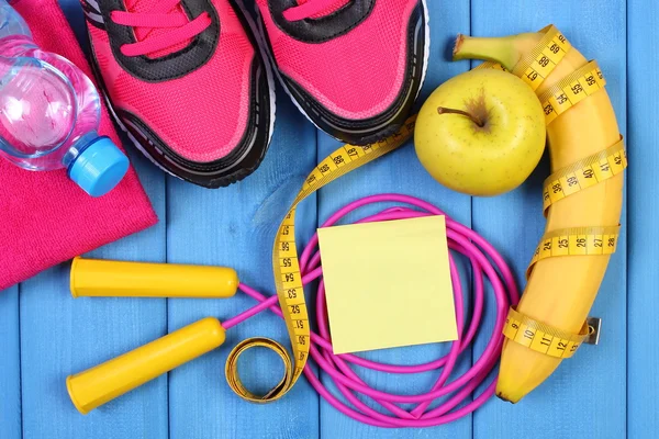 Pink sport shoes, fresh fruits and accessories for fitness on blue boards, copy space for text on sheet of paper