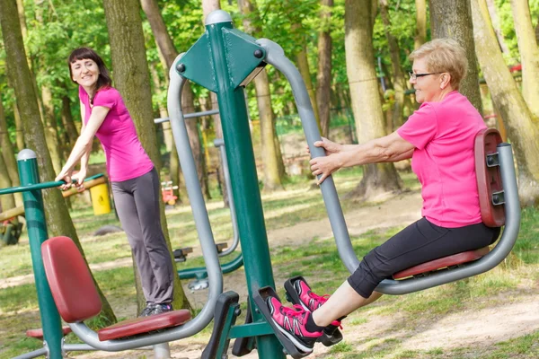Senior and young woman exercising lower body on outdoor gym, healthy lifestyle