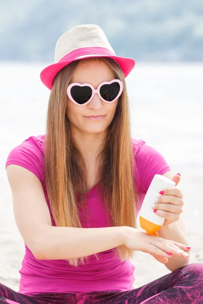 Happy girl in straw hat and sunglasses using sun lotion, sun protection on beach