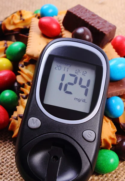 Glucometer with heap of sweets on jute burlap, diabetes and unhealthy food