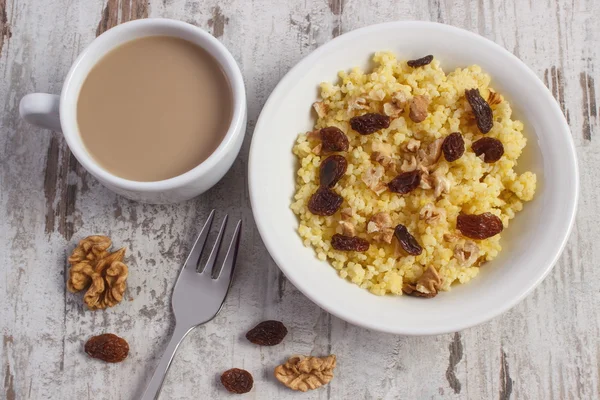 Cooked millet groats on white plate and cup of coffee with milk, healthy food and nutrition