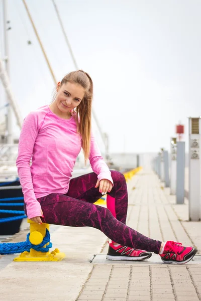 Slim girl in sports wear resting after exercise in seaport, healthy active lifestyle