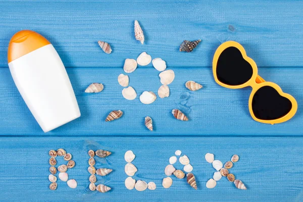 Word relax and shape of sun, sunglasses and sun lotion on blue boards, summer time