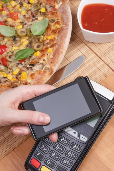 Using payment terminal and mobile phone with NFC technology for paying in restaurant, vegetarian pizza