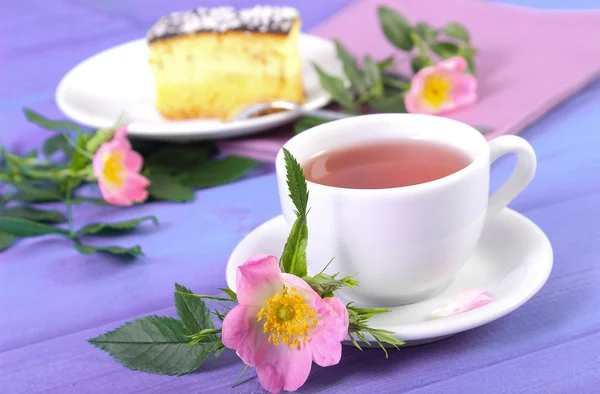 Cup of tea with cheesecake and wild rose flower on purple boards