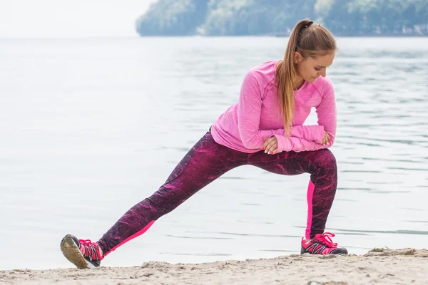 Slim girl in sporty clothes exercising on beach at sea, healthy active lifestyle