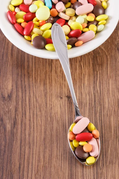 Medical pills on teaspoon and heap of colorful medical capsules on plate, health care concept