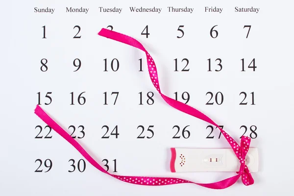 Pregnancy test with positive result wrapped ribbon on calendar, expecting for baby