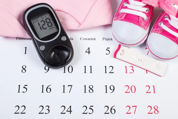 Pregnancy test with positive result, glucometer and clothing for newborn, checking sugar level, expecting for baby