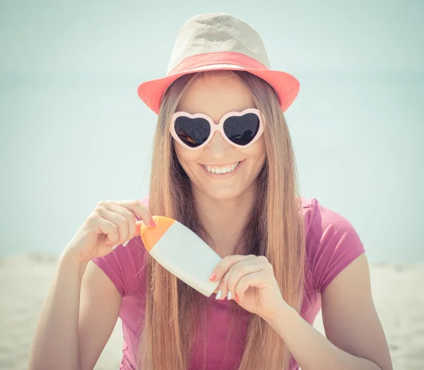 Happy girl in straw hat and sunglasses with sun lotion, sun protection on beach