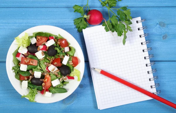 Fresh greek salad with vegetables and notepad for notes, healthy food