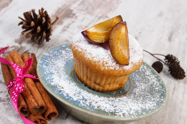 Muffins with plums and powdered sugar, cinnamon sticks on old wooden background, delicious dessert