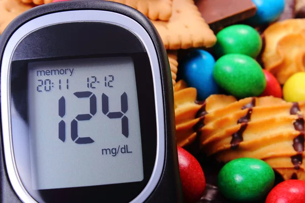 Glucometer with heap of sweets, diabetes and unhealthy food