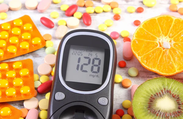 Glucose meter with result, fruits and colorful medical pills, diabetes, healthy lifestyle and nutrition