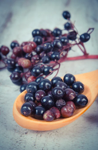 Vintage photo, Heap of elderberry with wooden spoon on old wooden background, healthy food