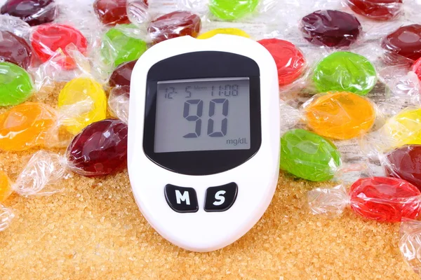 Glucometer, candies and granulated brown cane sugar, concept of diabetes