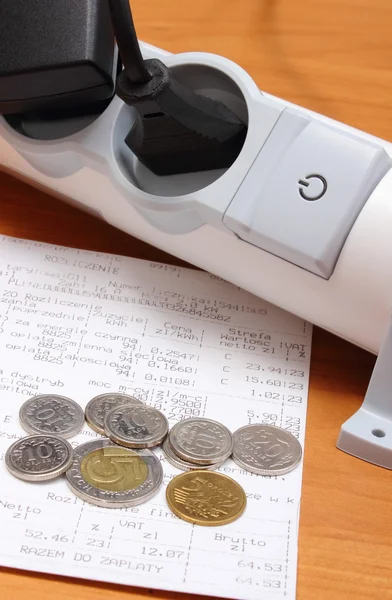 Electrical cords connected to power strip and electricity bill with coins