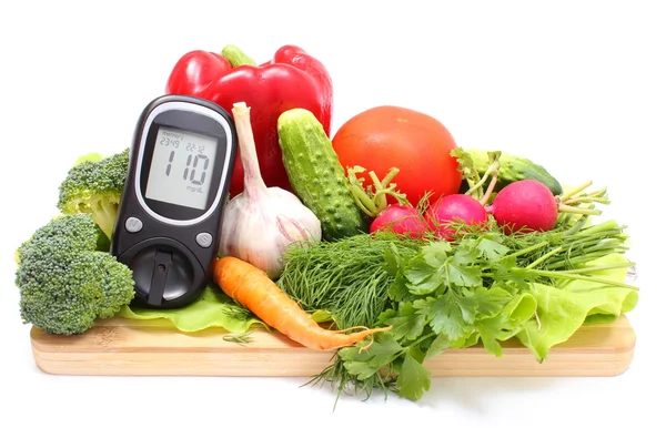 Glucose meter and fresh vegetables on wooden cutting board