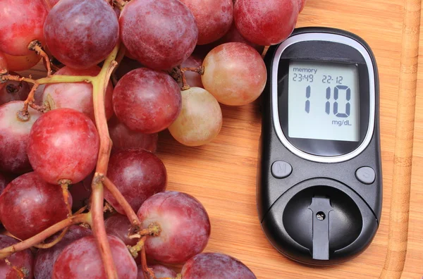 Glucose meter and fresh natural grapes on cutting board