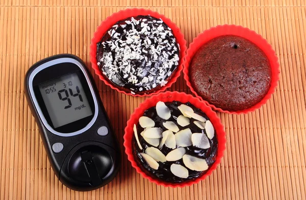 Glucose meter and chocolate muffins in red cups