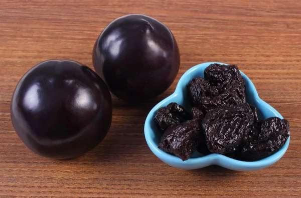 Fresh and dried plums in blue bowl on wooden table, healthy food