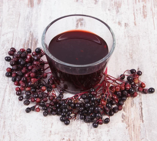 Bunch of fresh elderberry with juice on old wooden background, healthy nutrition