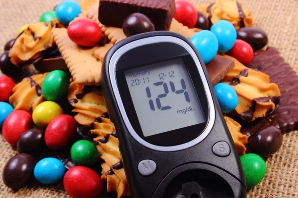 Glucometer with heap of sweets on jute burlap, diabetes and unhealthy food
