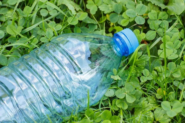 Plastic bottle of mineral water on grass in park, littering of environment