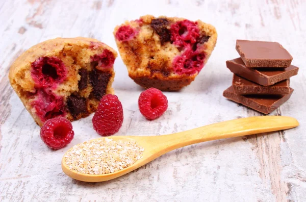 Muffins with raspberries, chocolate and oat bran on spoon, wooden background, delicious dessert