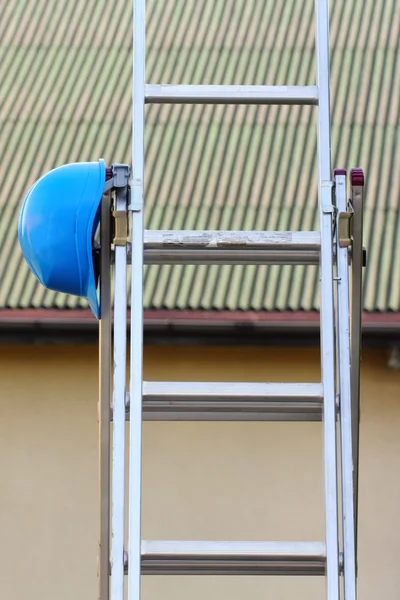 Protective blue helmet on aluminum ladder, safety at work