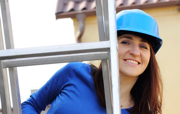 Smiling woman in blue helmet on aluminum ladder